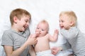 Two older brothers play and laugh with the youngest baby in a white bed. Happy childhood, big family Royalty Free Stock Photo