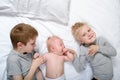 Two older brothers play and laugh with the youngest baby in a white bed. Happy childhood, big family Royalty Free Stock Photo