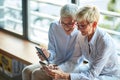 Two older business women of similar appearance have a good time watching the contents of smartphones during a break at workplace. Royalty Free Stock Photo