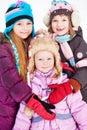 Two older girls embrace younger girl standing in winter park