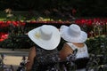 Two older women wearing wide white hats sitting together in a spa park full of colorful blooming flowers Royalty Free Stock Photo