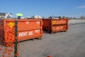 Two orange dumpsters at construction site on a wet sandy beach that say rent me on them