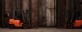 Two orange forklifts are parked side by side in a rustic-walled warehouse. Royalty Free Stock Photo