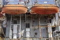 Two orange lifeboats hanging on rusty container ship.