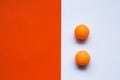 Two orange ping pong balls on an orange and white background.