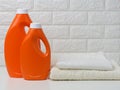 Two orange plastic bottles of liquid detergent and a stack of towels on a white shelf, home wash Royalty Free Stock Photo