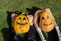 two orange pumpkins with painted grins and the bare feet of two children sitting on the grass