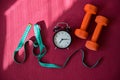 Two orange tunnels measuring tape and alarm clock on a pink yoga mat. Time to do fitness on and lose weight by the Royalty Free Stock Photo