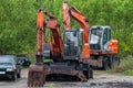 Two orange wheeled excavators near green forest