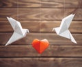 Two origami dove birds around red paper heart.