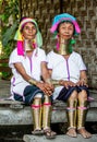 Two Padaung women in traditional dress and with metal rings around their neck are sitting next to each other in the village