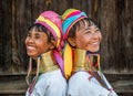 Two Padaung women in traditional dress and with metal rings around their neck stand next to each other.
