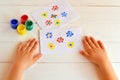 Two paintings of flowers painted children fingers. Jars with gouache. Children hands are on the table