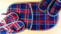 Two pair of of colorful comfortable, cushioned, checkered disposable slippers and another very large are on the wooden floor. Top