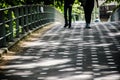 Two pair of legs walking over a bridge with sunlight making a pettern with shadows