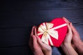 Two pairs of hands holding gift box in shape of heart on black w Royalty Free Stock Photo