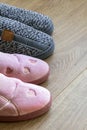 Two pairs of home slippers, gray mens and pink womens on a brown wooden floor. Cozy, warm and comfortable domestic shoes Royalty Free Stock Photo