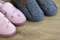 Two pairs of home slippers, pink womens and gray mens on a brown wooden floor. Cozy, warm and comfortable domestic shoes Royalty Free Stock Photo