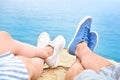 Two pairs of legs, male and female, first person view. Tourists resting on a rock against the background of the sea