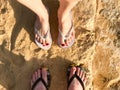 Two pairs of male and female legs with a manicure in slippers, a foot with fingers in flip-flops on a stone sandy floor, earth, be Royalty Free Stock Photo