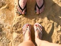 Two pairs of male and female legs with a manicure in slippers, a foot with fingers in flip-flops on a stone sandy floor, earth, be Royalty Free Stock Photo