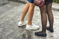 Two pairs of slim girls legs in short skirts, white leather sneakers and comfortable summer shoes on low platform. Fashion, style Royalty Free Stock Photo