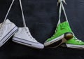 two pairs of used textile shoes hang on a black background, close up
