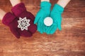 Two pairs of women hands knitted mittens holding a Christmas toy on a wooden background.