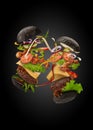 Two palatable black burgers with flying ingredients on black background. Ham, beef cutlet, cheese, sauces, vegetables Royalty Free Stock Photo