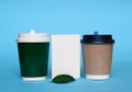 Two paper cups for coffee and tea, green ficus leaf and a white cardboard card. Royalty Free Stock Photo