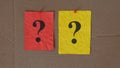 Two paper notes with question marks on them pinned to a cardboard surface.