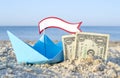 Two paper one dollars bills half buried in sand, blue paper boat Royalty Free Stock Photo