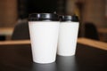 Two paper white cups with a plastic black lid for takeaway coffee on a black background of the table Royalty Free Stock Photo
