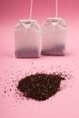 Two paper white tea bags and a handful of black tea on a pink background close-up