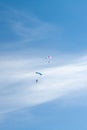 Two parachutists soar on colorful parachutes across the boundless blue sky against the background of white fluffy clouds Royalty Free Stock Photo