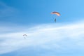 Two parachutists soar on colorful parachutes across the boundless blue sky against the background of white fluffy clouds Royalty Free Stock Photo