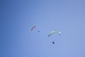 Two paragliders on colored parachutes fly against a clear blue sky