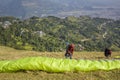 Two paragliders prepare parachutes for takeoff on the hillside against the backdrop of the city in a green mountain valley