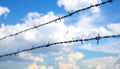 Two strands of barbed wire fence against a bright blue sky with scattered clouds metal spikes Royalty Free Stock Photo