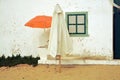 Two parasols. White and orange. Portugal. Atlantic beach. Old house. Window. Door. Sand. Grass. Travel. Touring. Wall. Green. Royalty Free Stock Photo