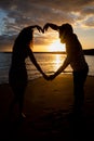 Two partners on the beach make a heart with their arms during the sunset, passionate and romantic moment Royalty Free Stock Photo