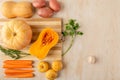Two parts of a cut pumpkin, a round pumpkin, potatoes, turnips, carrots and garlic are laid out on a bamboo cutting Board and a
