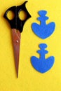 Two parts in the shape of an anchor cut from blue felt. The scissors on the yellow wool background. Step. Closeup. Top view Royalty Free Stock Photo