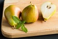 Two pears and piece of a pear with fresh basil leaves on a wooden cutting board, side view