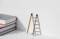 Two pencils and shadow in form of ladder with stack of textbooks on white tabletop