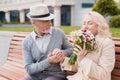 Two pensioners are sitting on a bench in the alley. The aged man gave the woman flowers. He holds her hand Royalty Free Stock Photo