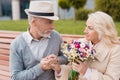 Two pensioners are sitting on a bench in the alley. The aged man gave the woman flowers. He holds her hand Royalty Free Stock Photo