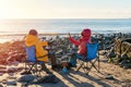 Two people on beach chairs together on winter beach, sunny, blue sky horizon. British cold winter. Local tourism concept