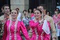 two people in bright pink dresses and white feathers smile and walk along the street