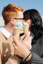 Two people in love sitting outdoors, holding ice cream, sensually kissing